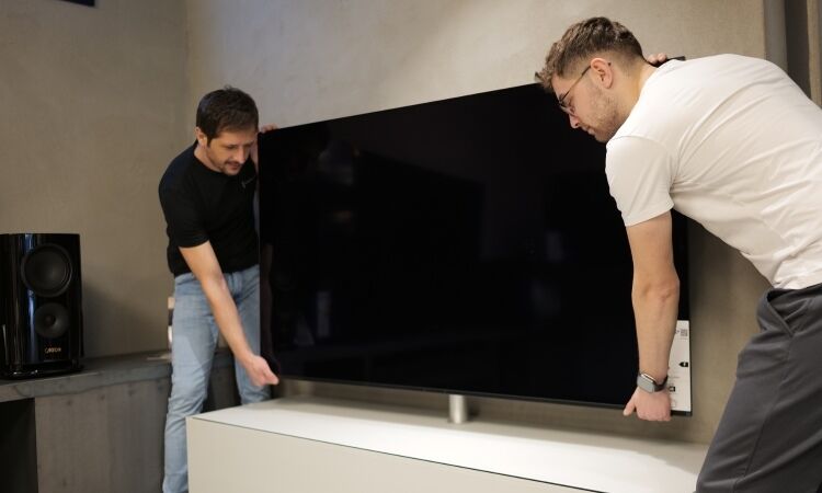 Elvis Suljic und Moritz Riebow heben einen Fernseher an die Wand Elvis Suljic und Moritz Riebow heben einen Fernseher an die Wand